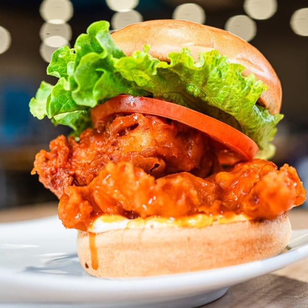 Spicy fried chicken sandwich with lettuce and tomato on a bun, served on a white plate.