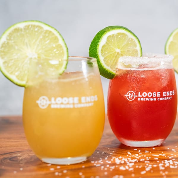Two Loose Ends Brewery cocktails, one yellow and one red, garnished with lime slices and salt.