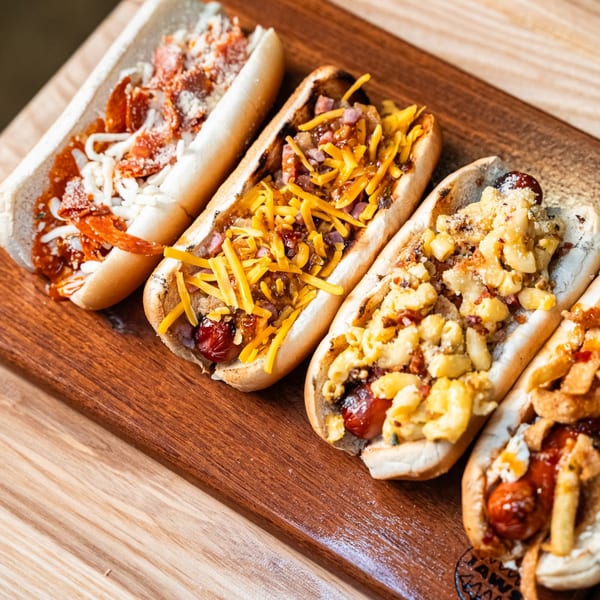 Four gourmet hot dogs with diverse toppings, including pepperoni, cheese, mac and cheese, and fries.