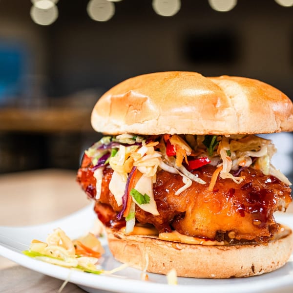 Loose Ends Brewery's crispy chicken sandwich with slaw and sauce on a white plate.
