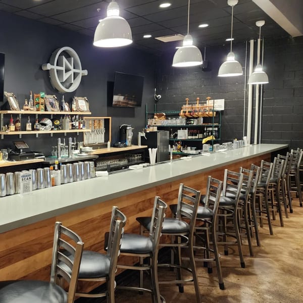 A long, modern bar with stools, shelves of bottles, and brewing equipment at Loose Ends Brewery.