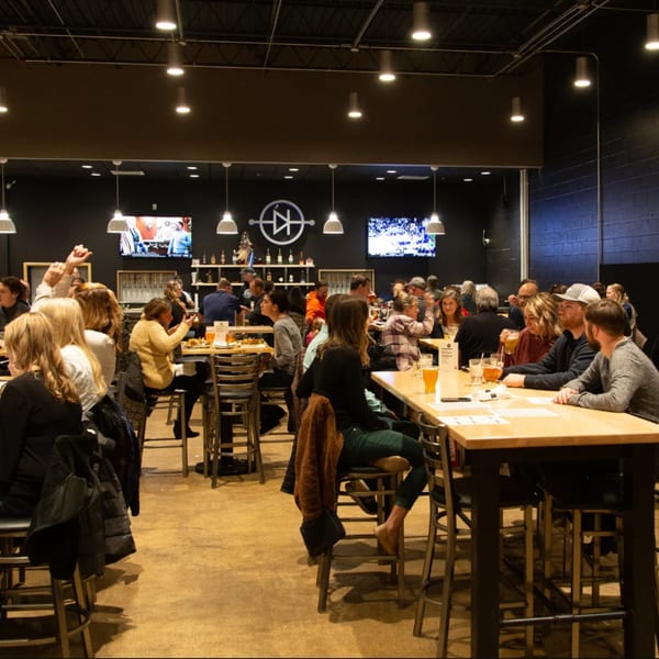 Patrons enjoying drinks and food at high-top tables in the spacious Loose Ends Brewery taproom.