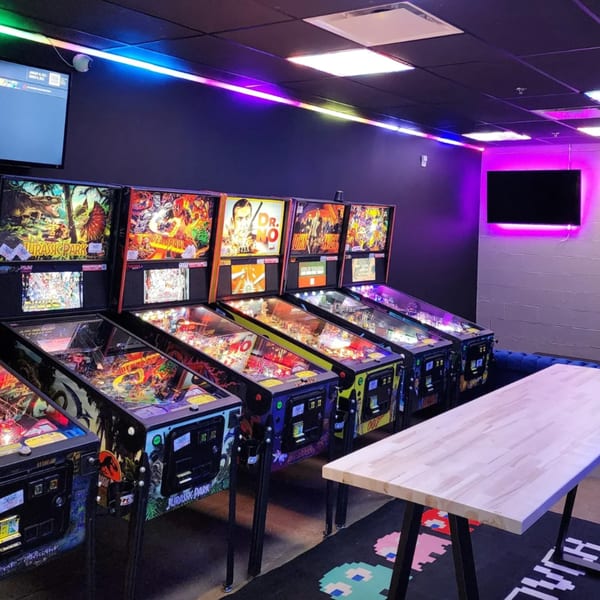 A row of pinball machines with colorful displays under neon lights at Loose Ends Brewery.