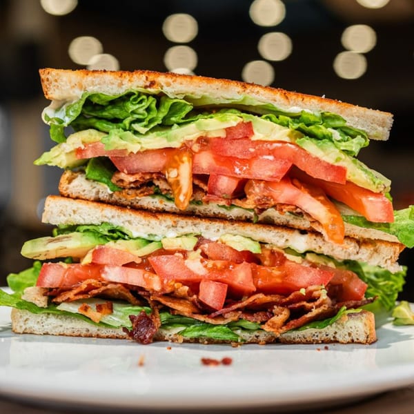 A towering BLT sandwich with bacon, lettuce, avocado, and tomatoes on toasted bread.
