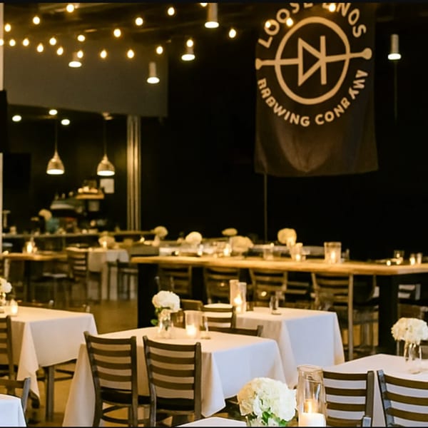 Interior of Loose Ends Brewery with tables set with white tablecloths, flowers, and candles under string lights.