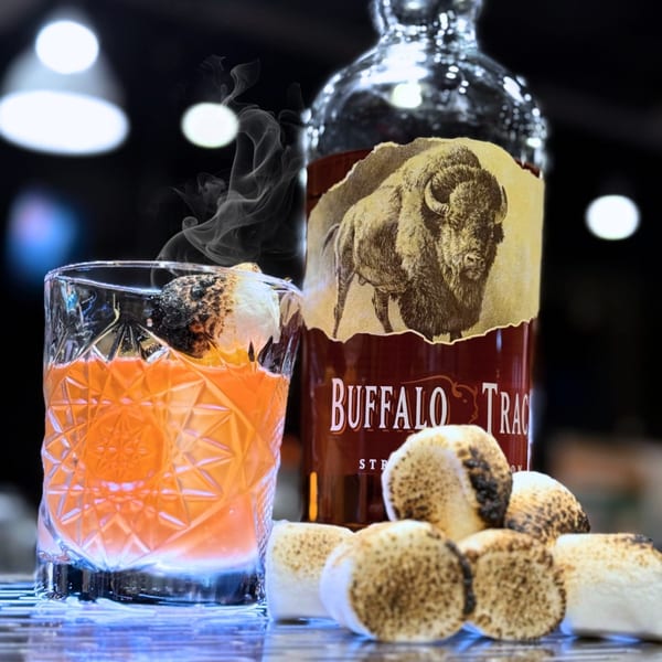 Smoky orange cocktail with a charred marshmallow, Buffalo Trace bottle, and toasted marshmallows.